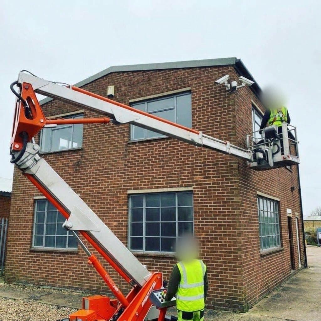 Illustration of a tracked cherry picker being used for high-level work on a brick building