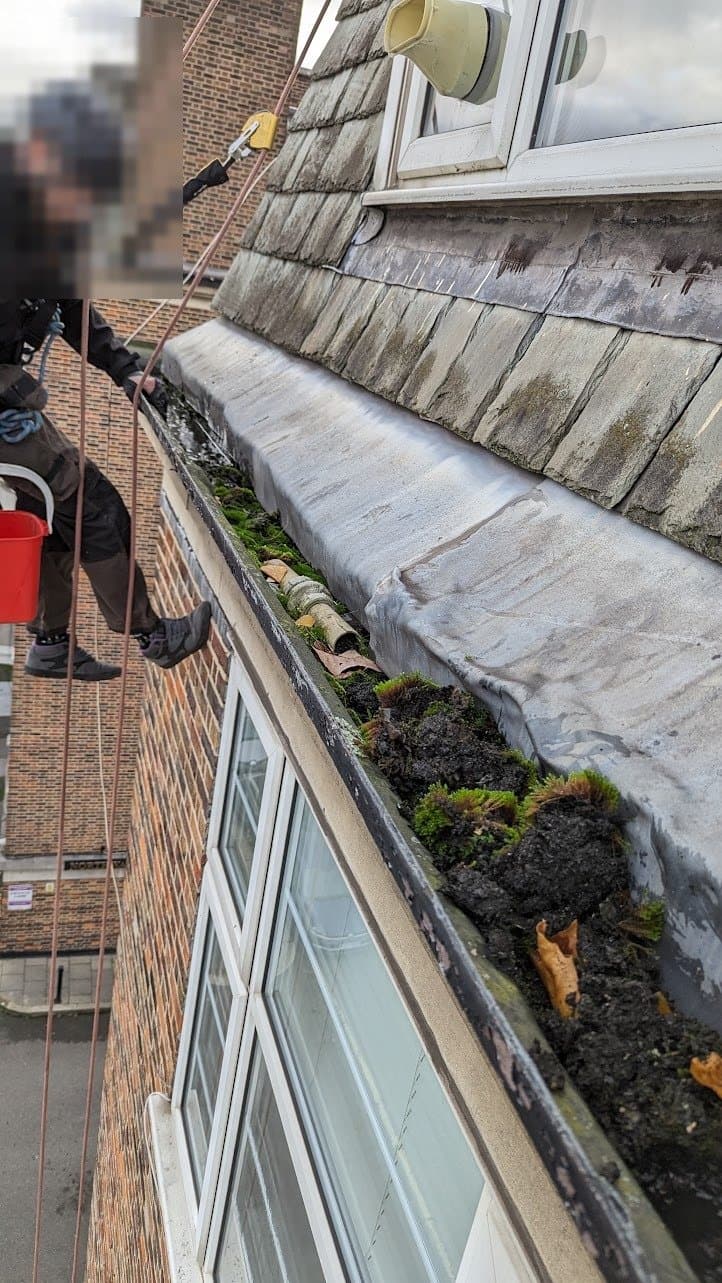 Rope access technician with a bucket working the concealed parapet gutter
