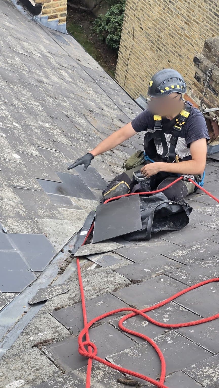 Technician on the slate slope with replacement slates and a slate ripper beside him