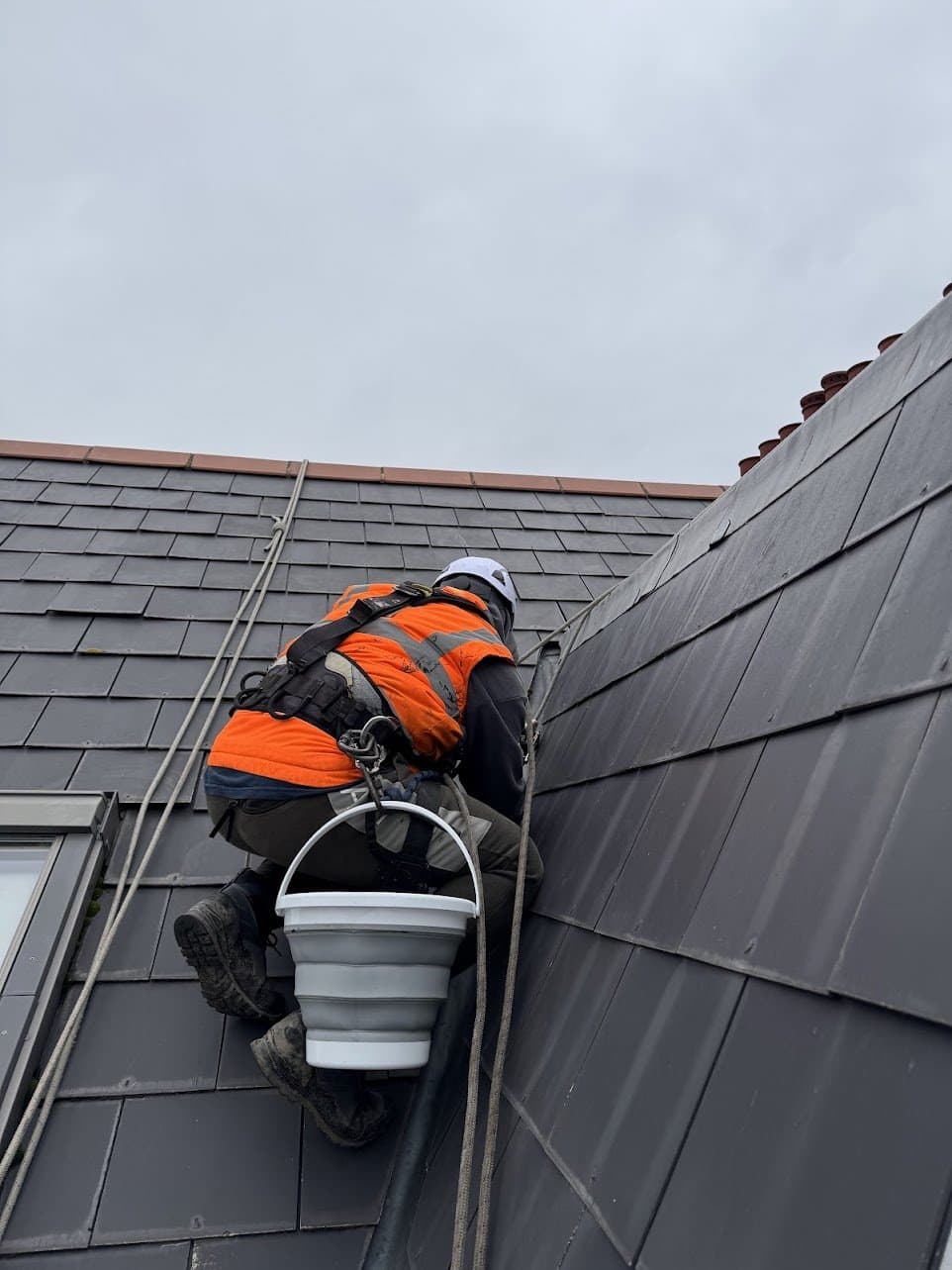 Technician part way up the tiled slope on two ropes with a bucket clipped to the harness