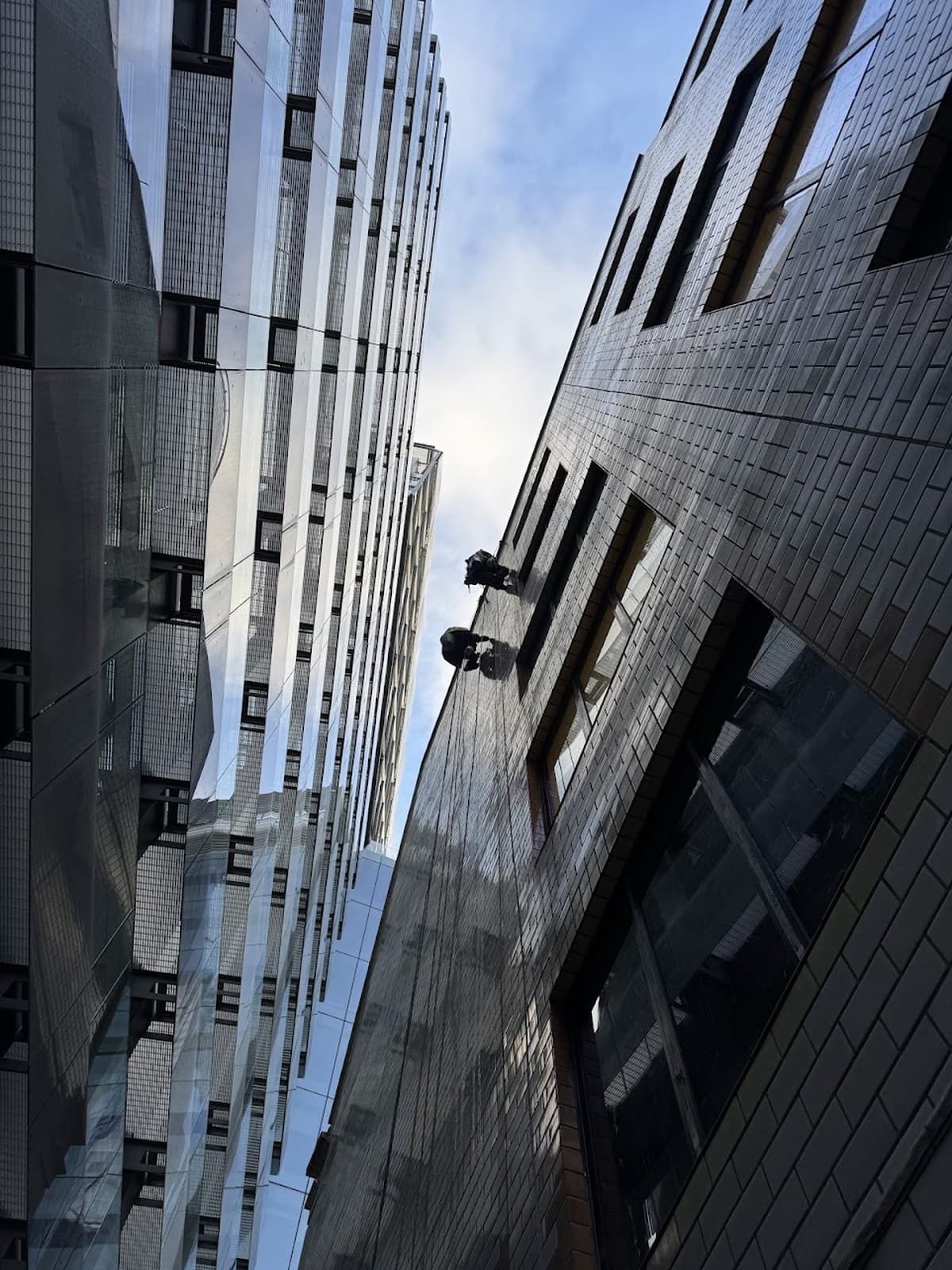 Two Innova rope access technicians suspended in a narrow alley between glass towers in the City of London