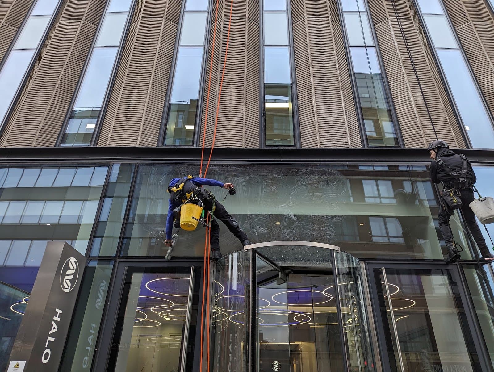 Technician soaping the entrance canopy glazing at the HALO building with the revolving door in use