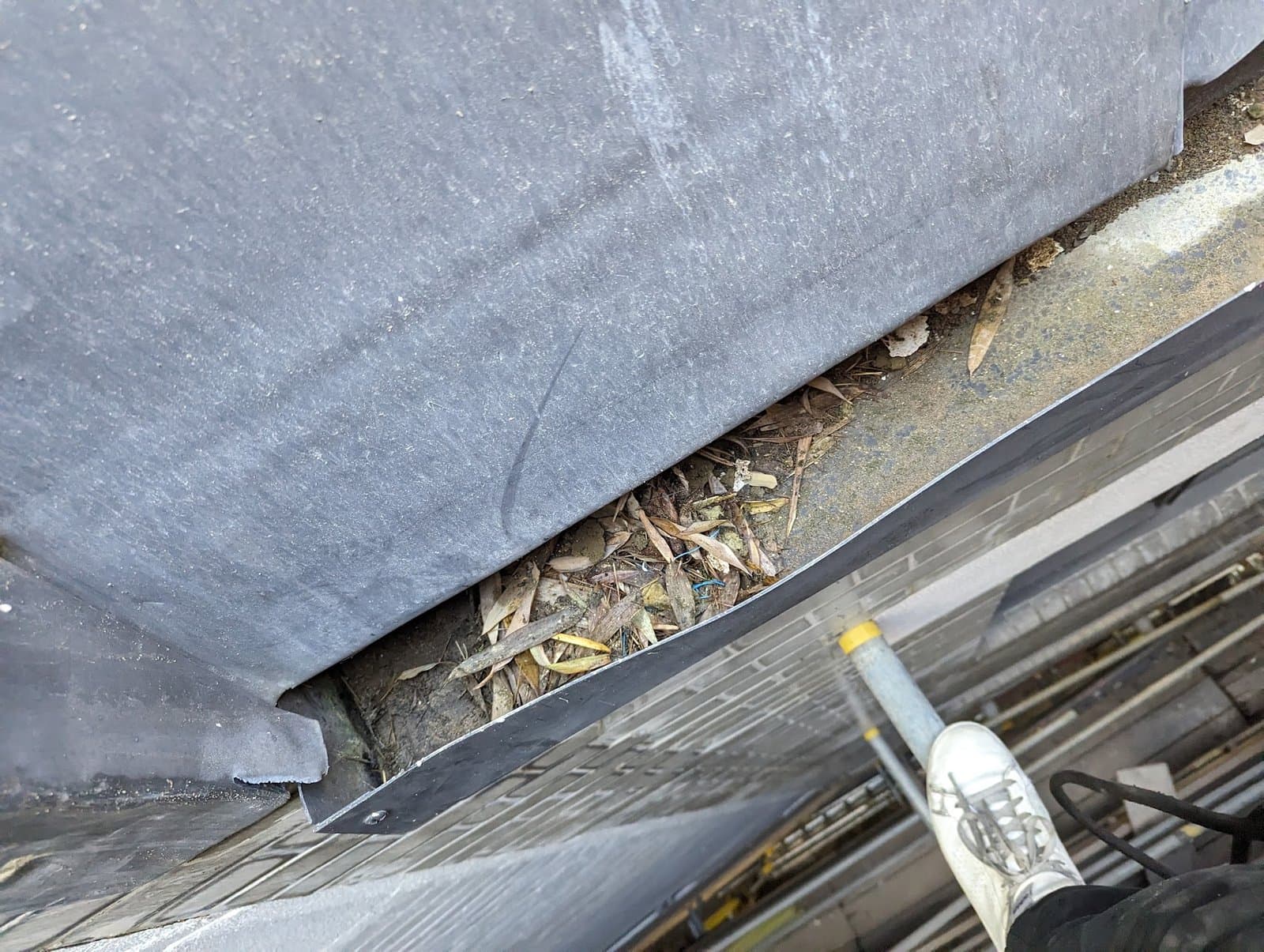 Before: debris packed under the lead flashing, blocking the gutter