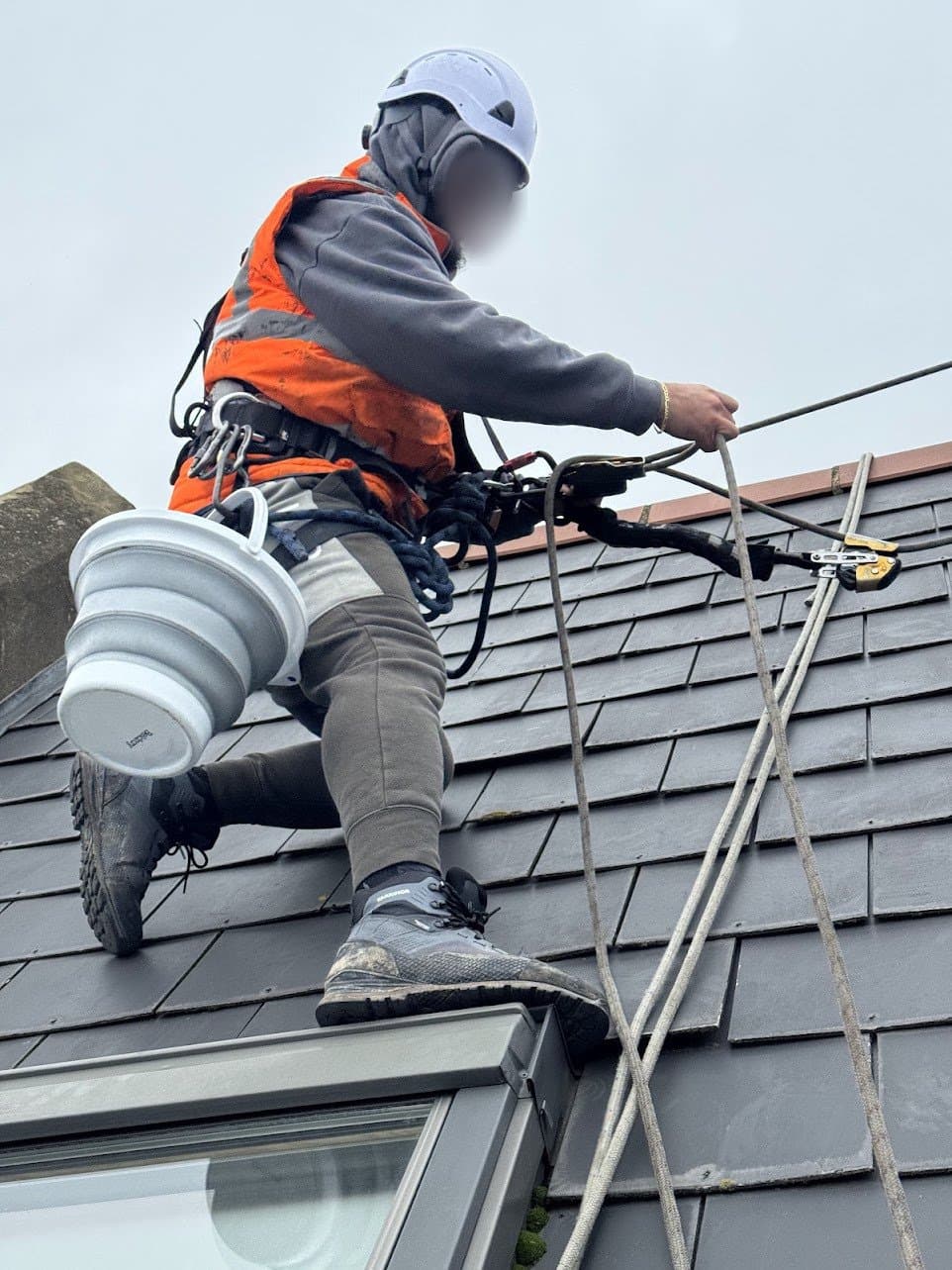 Innova rope access technician in helmet, hi-vis and full harness, roped in while repairing a pitched roof